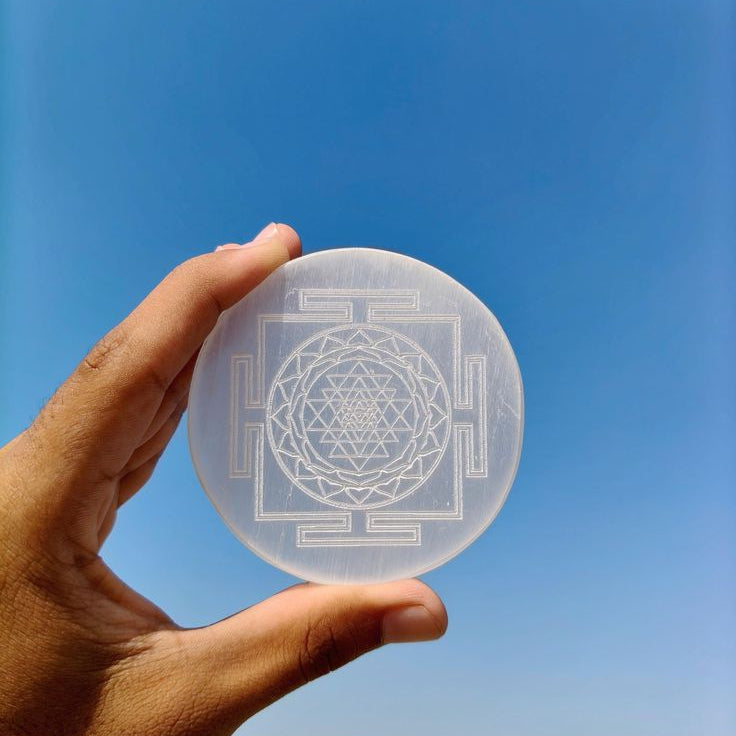 A persons hand holding selenite plate with shree yantra carving