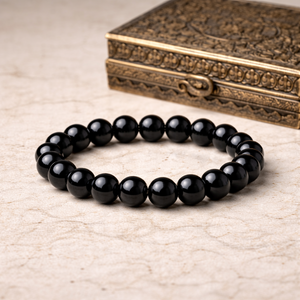 Black obsidian bracelet on a textured surface with an ornate box in the background