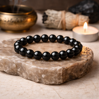 Black beaded bracelet on a stone surface with a candle and incense in the background