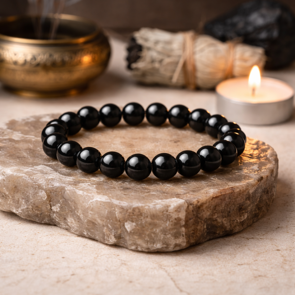 Black beaded bracelet on a stone surface with a candle and incense in the background