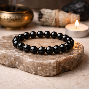 Black beaded bracelet on a stone surface with a candle and incense in the background