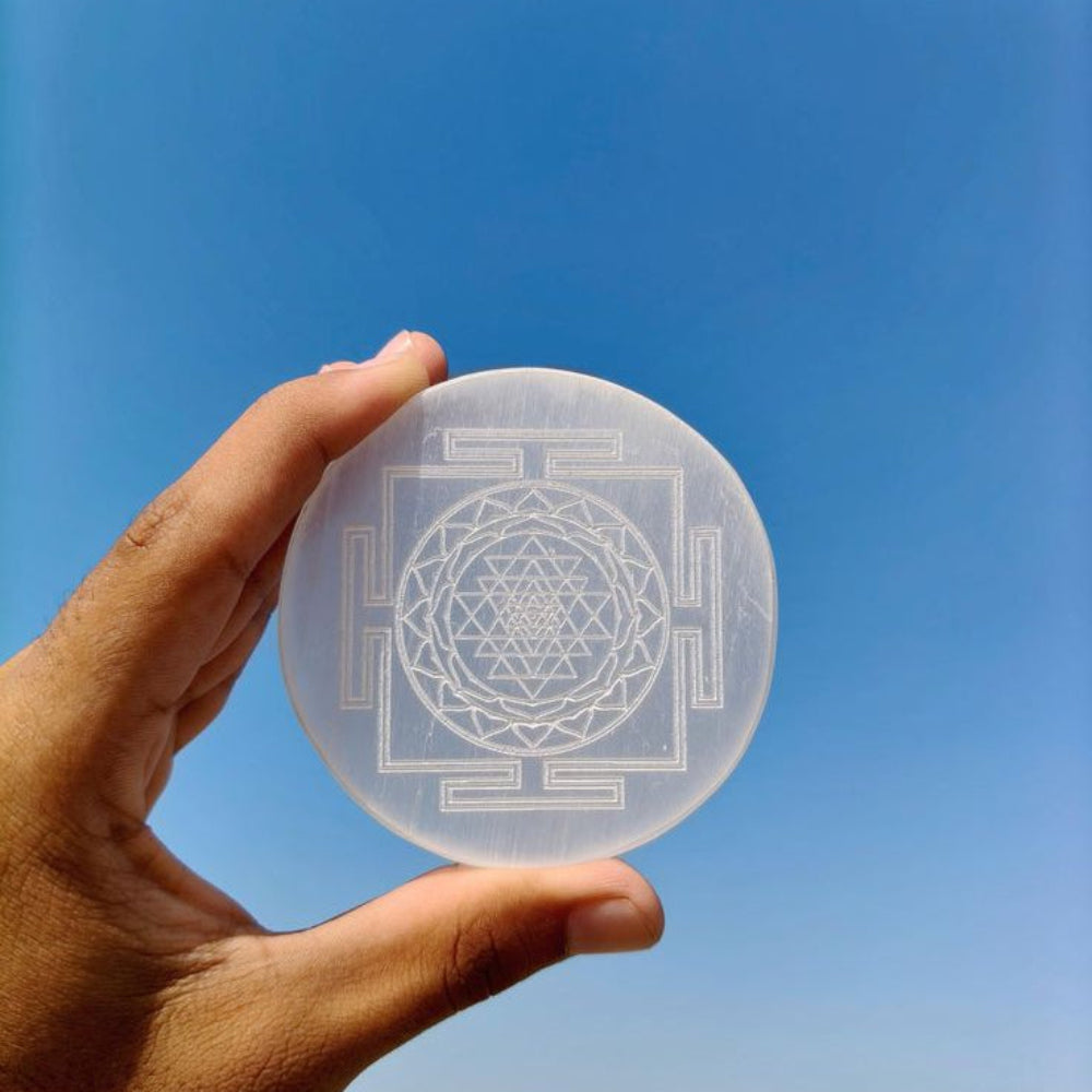 A persons hand holding selenite plate with shree yantra carving