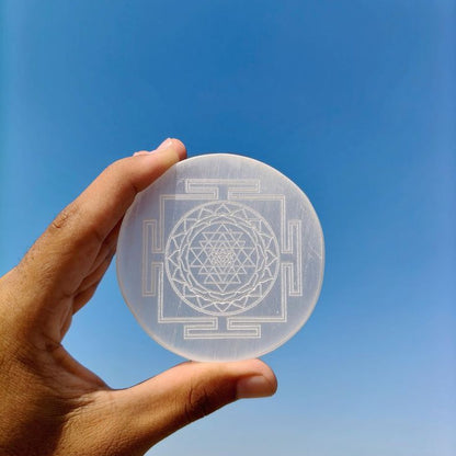 A persons hand holding selenite plate with shree yantra carving