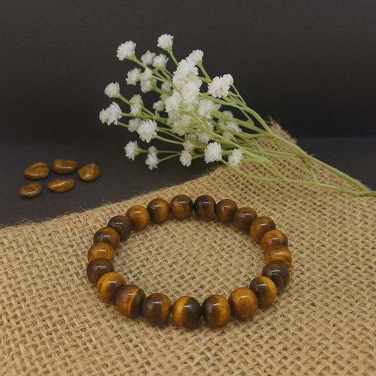 Brown beaded bracelet on a textured surface with white flowers in the background
