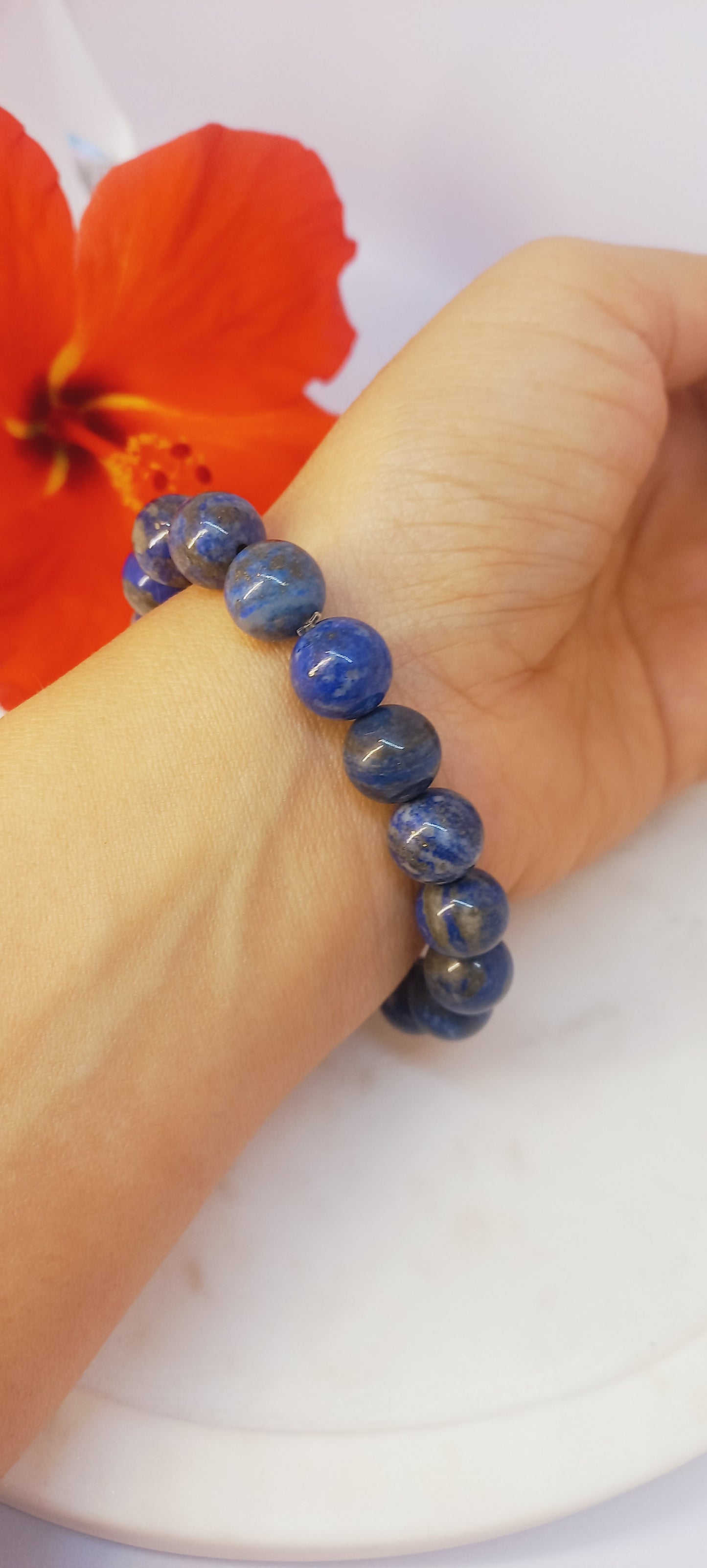 Blue beaded bracelet on a wrist with a red flower in the background